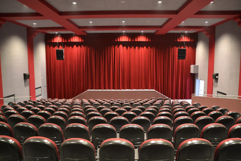 zdjecie przedstawia salę kinową w Gminnym Centrum Kultury w Trzebnicy, na pierwszym planie rzędy krzeseł dla widowni, w tle scena i czerwona kurtyna
